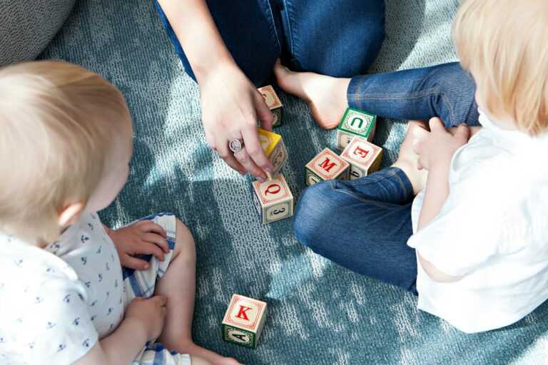 Children build with colorful blocks on a floor while an adult observes and talks with them.