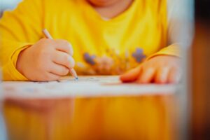 Child uses playdough, crayons, and child-safe scissors at a kitchen table during a hands-on activity.