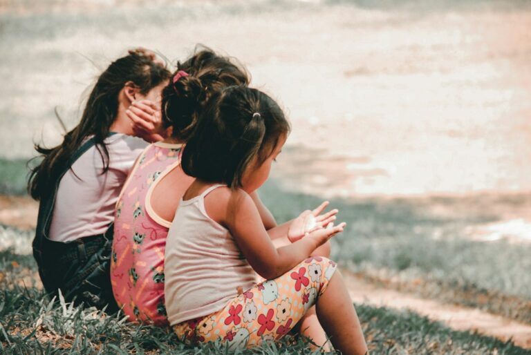 Preschool child hugs a caregiver at classroom drop-off while a teacher welcomes them nearby.