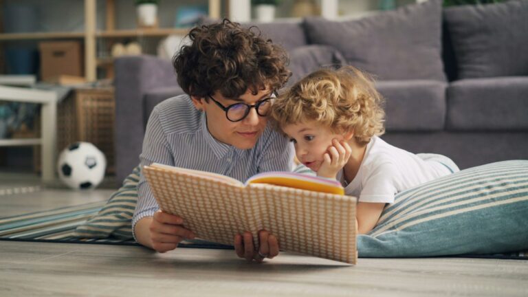 Adult and young child look at a picture book together in a bright home reading space.